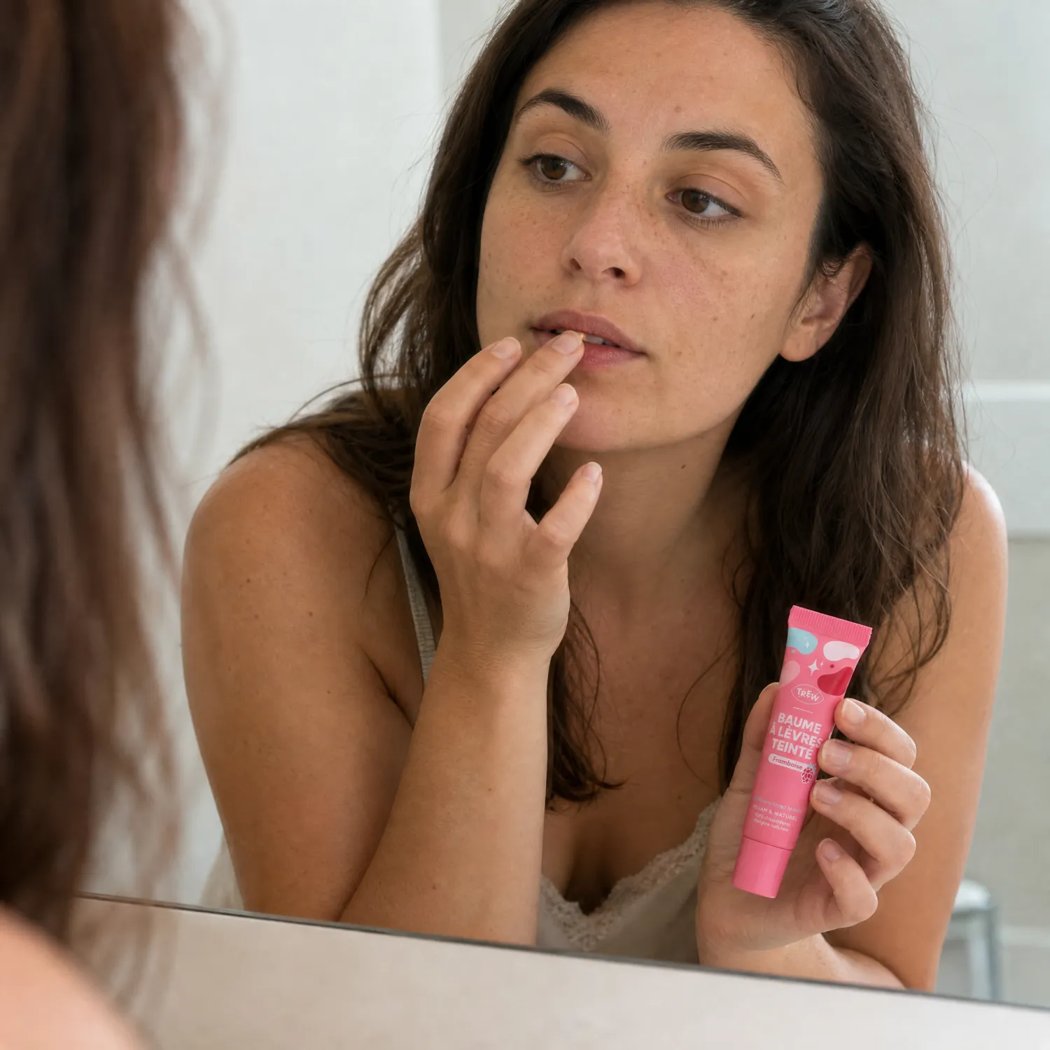 Femme appliquant un baume à lèvres teinté rose devant un miroir