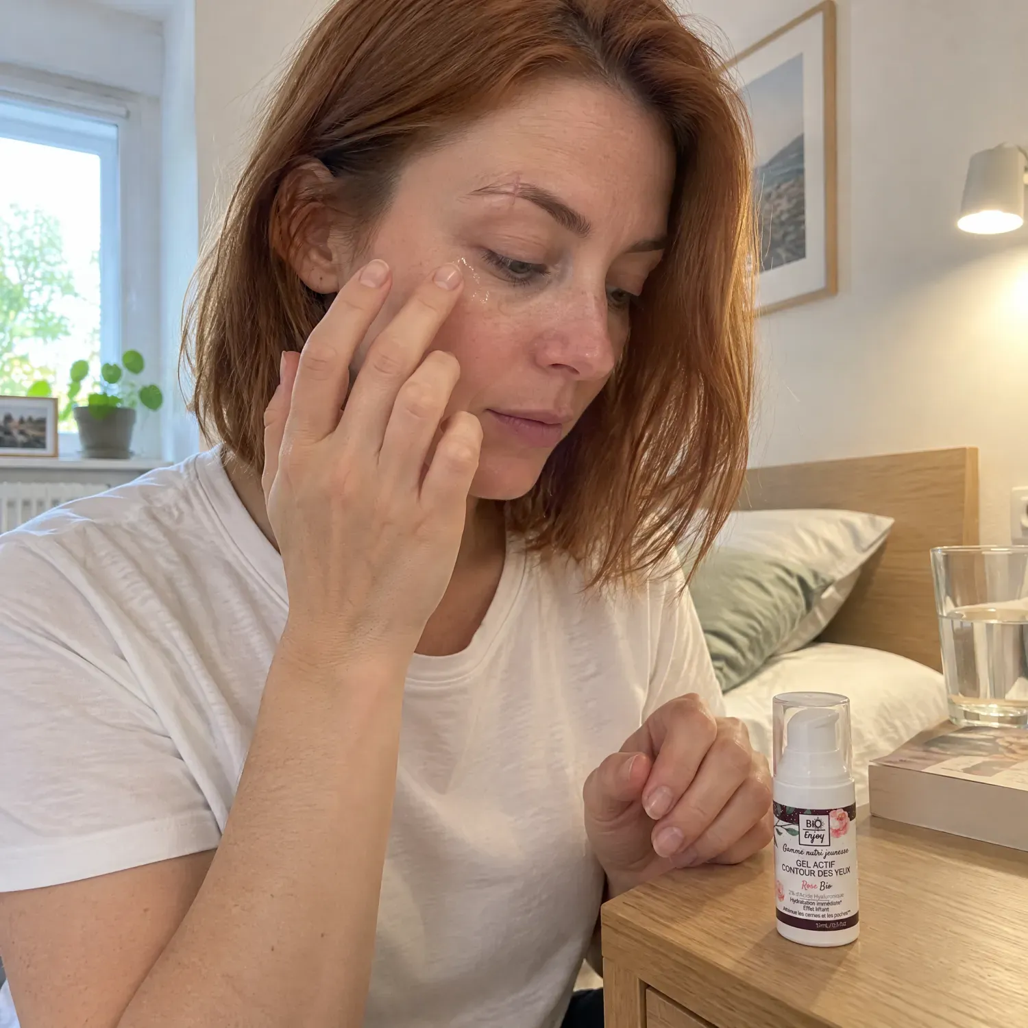 Femme rousse appliquant un gel contour des yeux à la rose bio du bout des doigts