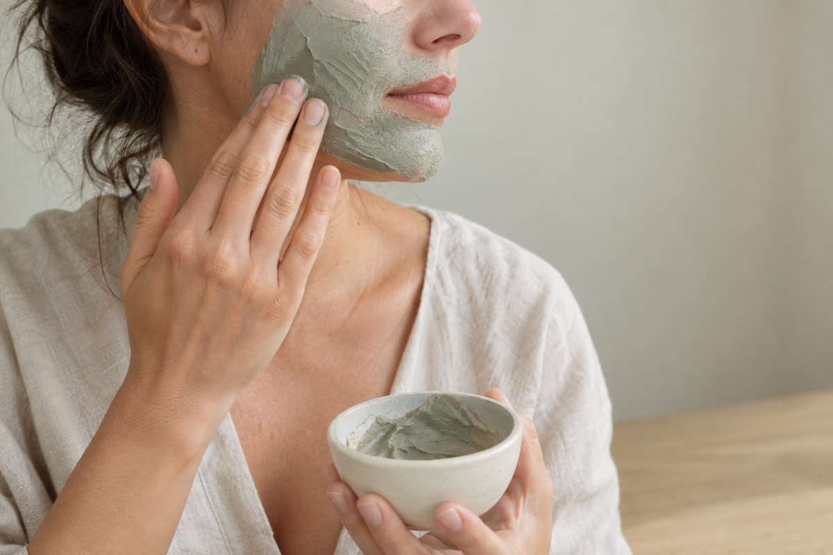 Femme appliquant un masque à l'argile verte sur le visage avec un bol